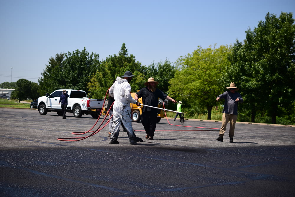 Crew hand-applying hot rubber crack sealant on asphalt